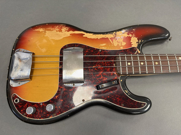 Vintage sunburst electric bass guitar with worn finish and tortoiseshell pickguard, showing metal pickup covers and control knobs, photographed on gray background