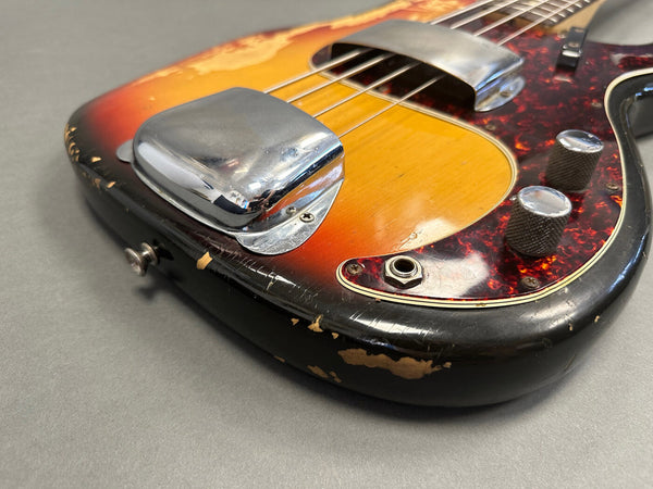 Close-up of vintage sunburst electric bass guitar body with chrome pickups, tortoiseshell pickguard, and worn black edges on gray background