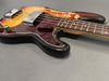 Close-up of vintage electric bass guitar body with sunburst finish, tortoiseshell pickguard, and metal bridge covers on gray background