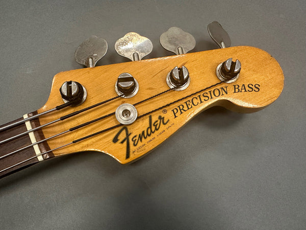 Close-up of Fender Precision Bass headstock with tuning pegs and strings on gray background