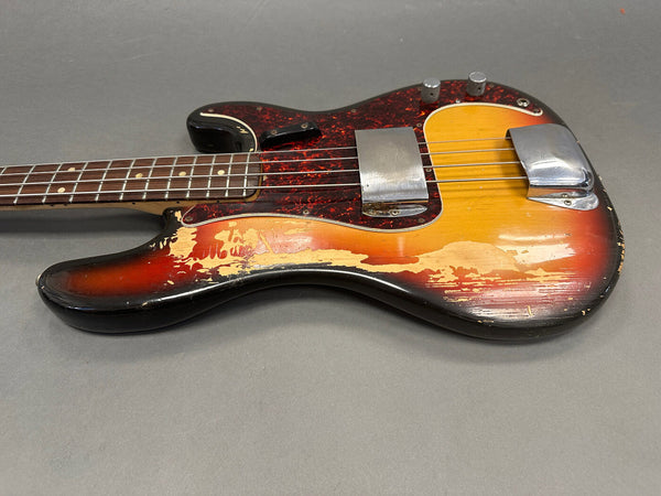 Worn vintage sunburst electric bass guitar with tortoiseshell pickguard and chrome bridge covers on gray background