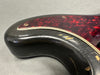 Close-up of black electric guitar body with tortoiseshell pickguard showing paint chips and scratches on the lower horn and edges
