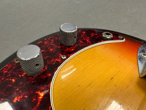 Close-up of vintage electric guitar with tortoiseshell pickguard and knurled metal control knobs on sunburst finish body