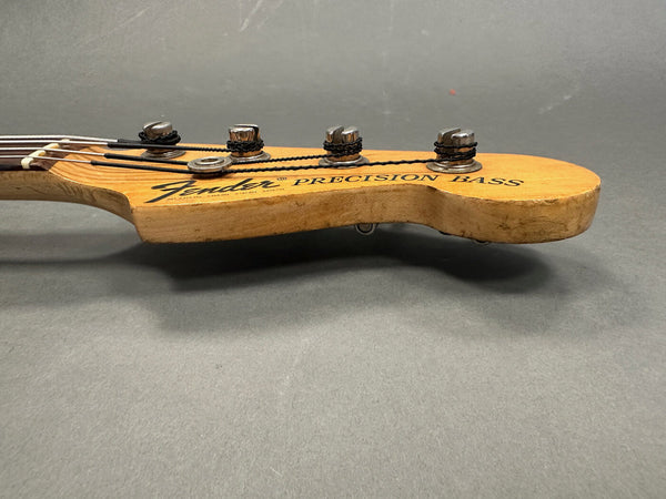 Close-up of Fender Precision Bass natural wood headstock with tuning pegs and strings on gray background