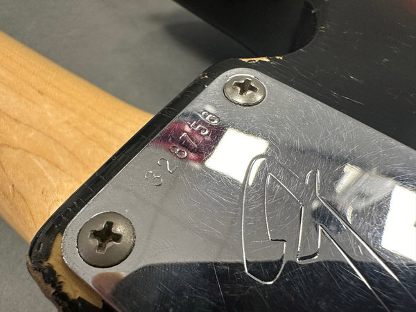 Close-up of vintage Fender guitar neck plate with serial number 328756, showing wear and screws on a black guitar body and maple neck wood.