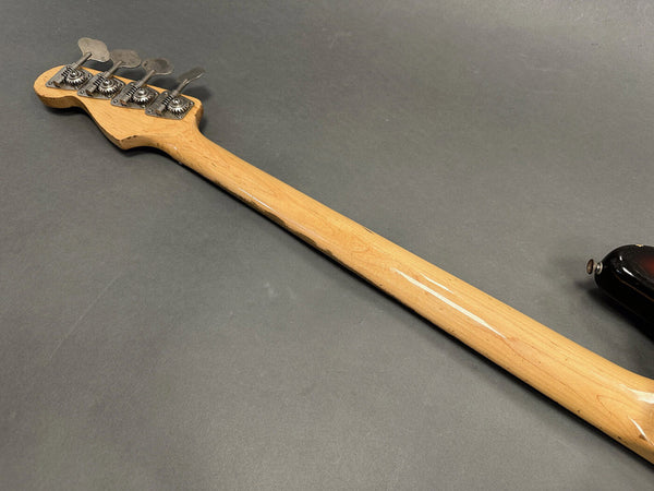 Maple neck and vintage chrome tuning pegs of a bass guitar against a gray background, showing detailed wood grain and wear marks.