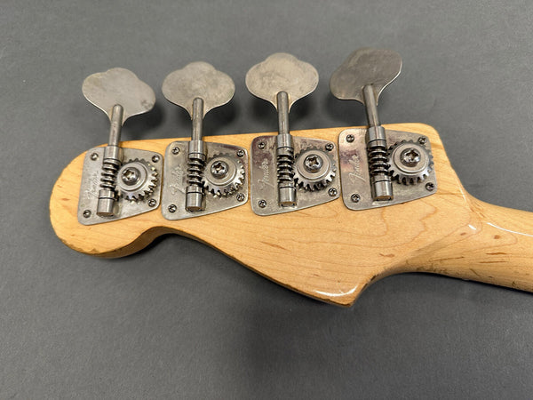 Close-up of vintage Fender bass guitar tuning pegs on natural wood headstock against gray background
