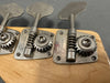 Close-up of vintage Fender bass guitar tuning pegs on maple headstock with metal gear mechanisms and engraved Fender logo