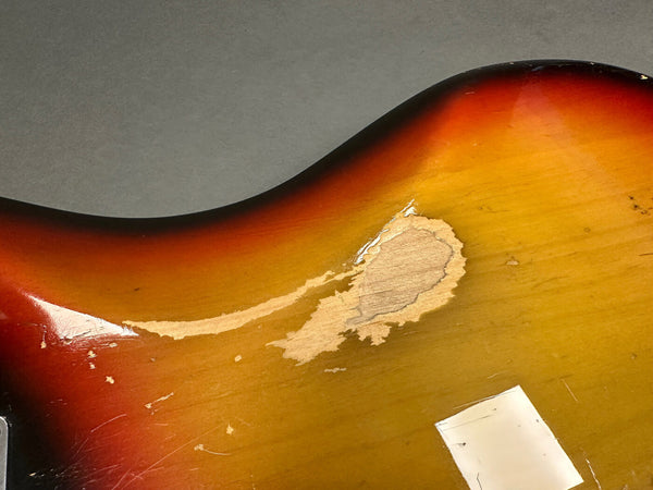 Close-up of sunburst electric guitar body showing worn and chipped finish with wood exposed on gray background