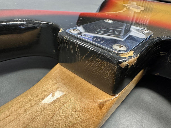 Close-up of vintage electric guitar neck joint showing worn black finish, sunburst body, and metal neck plate with serial number 328760.