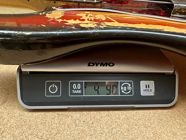 Close-up of a worn electric guitar body placed on a DYMO digital scale showing a weight of 4.90 pounds.
