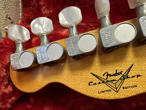 Close-up of Fender Custom Shop Limited Edition guitar headstock with vintage style tuners and pearloid tuning pegs on red plush guitar case lining.