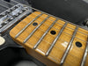 Close-up of electric guitar maple fretboard with metal frets and black dot inlays, showing strings and part of black guitar body and chrome pickup.