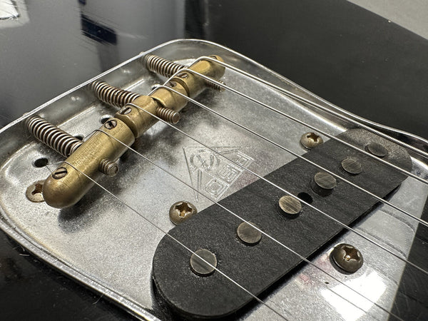 Close-up of vintage electric guitar bridge and single coil pickup with metal plate and six strings on black guitar body