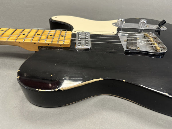 Close-up of worn black electric guitar body with cream pickguard, maple neck, and chrome bridge and pickup hardware on gray background