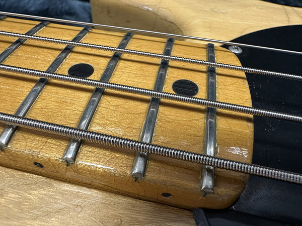 Close-up of vintage electric bass guitar fretboard with metal frets, dot inlays, and round wound strings on natural wood finish