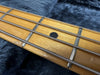 Close-up image of vintage bass guitar maple fretboard with metal frets and wound strings on dark fabric background