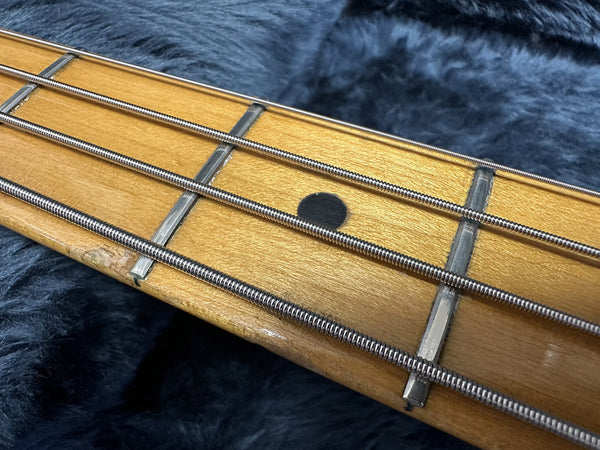 Close-up image of vintage bass guitar maple fretboard with metal frets and wound strings on dark fabric background