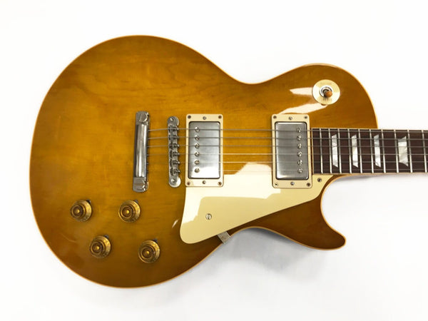 Close-up of honey burst electric guitar body with dual humbucker pickups, chrome bridge, cream pickguard, and four gold control knobs on white background