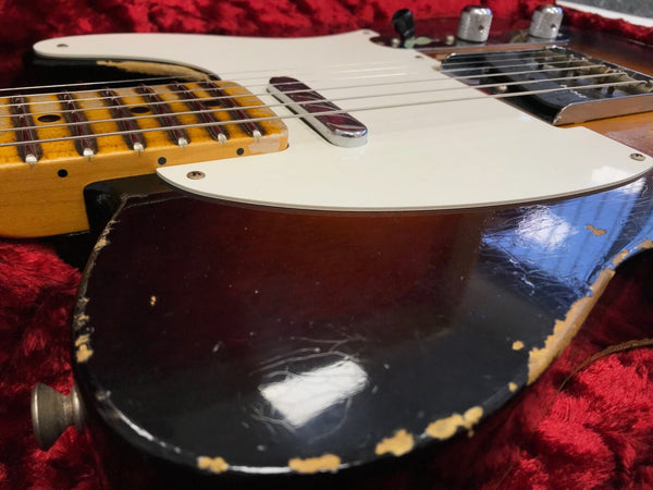 Close-up of vintage electric guitar body with worn black finish, white pickguard, and maple neck resting on red plush case interior