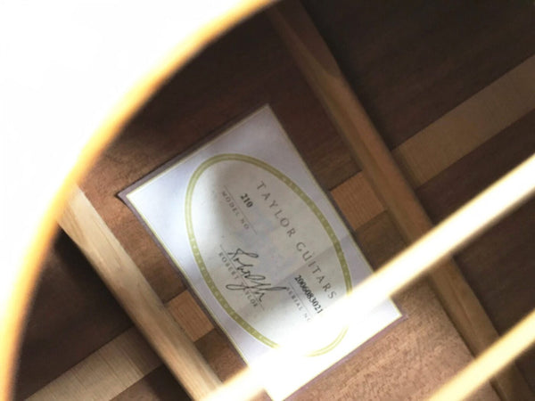 Close-up view of Taylor Guitars model 210 label inside acoustic guitar body with wooden bracing visible