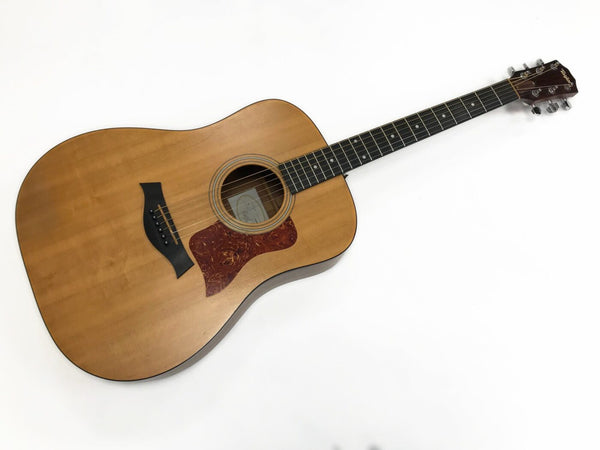 Taylor acoustic guitar with natural wood finish, tortoiseshell pickguard, and black bridge pins on white background