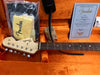 Fender Stratocaster guitar headstock and neck in orange plush case with Fender certificate of authenticity, cleaning cloth, strap, and accessories.