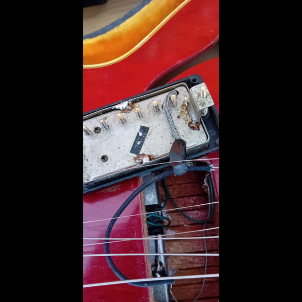 Close-up of vintage guitar humbucker pickup with exposed wiring mounted on red electric guitar body showing pickup cavity and strings.