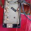 Close-up of vintage guitar humbucker pickup with exposed wiring and metal cover on red electric guitar body