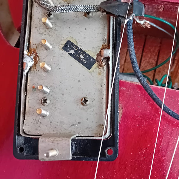 Close-up of vintage guitar humbucker pickup with exposed wiring and metal cover on red electric guitar body