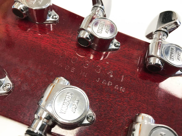 Close-up of Yamaha guitar tuning pegs on red wood headstock with "Made in Japan" stamp and serial number visible