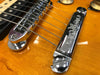 Close-up of guitar bridge and tailpiece on amber electric guitar with chrome hardware and strings