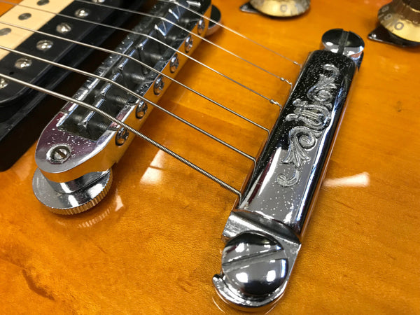 Close-up of guitar bridge and tailpiece on amber electric guitar with chrome hardware and strings