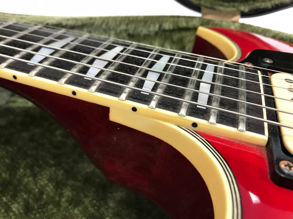 Close-up of electric guitar fretboard and strings on red guitar body with cream binding and inlays on a green textured surface