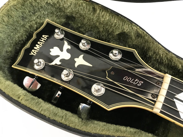 Close-up of Yamaha SG700 guitar headstock with tuning pegs and decorative inlay inside green plush guitar case lining