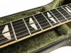 Close-up of electric guitar fretboard with trapezoid inlays and metal strings inside green plush-lined guitar case