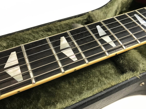 Close-up of electric guitar fretboard with trapezoid inlays and metal strings inside green plush-lined guitar case